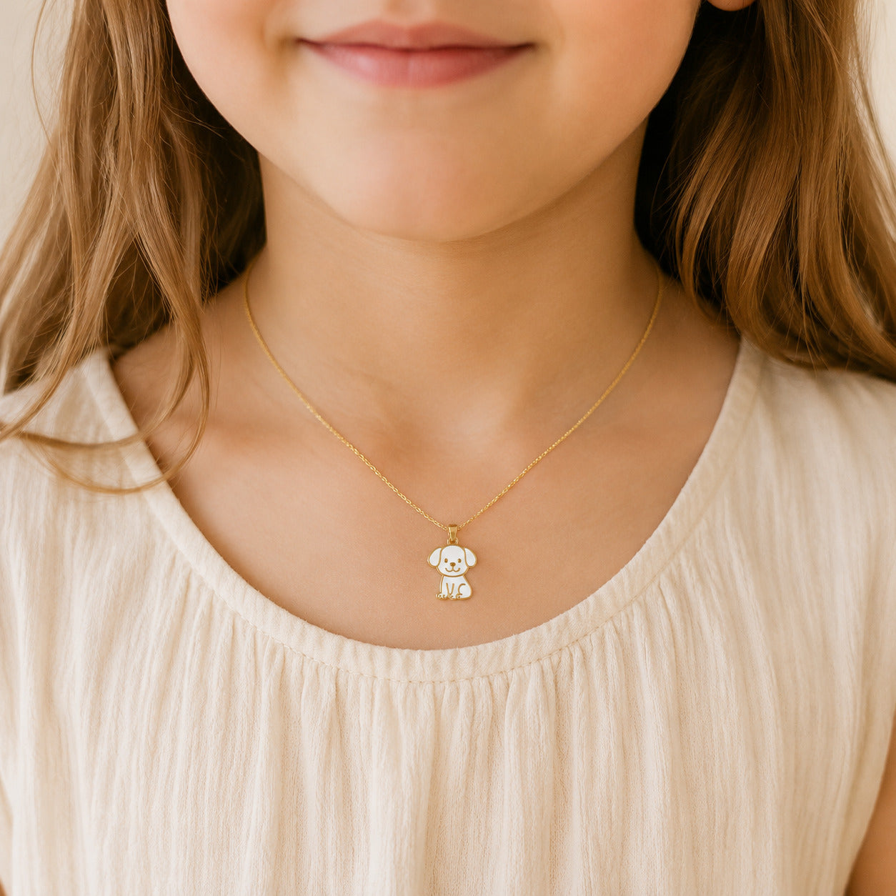 A close-up of a child wearing a delicate gold necklace with a small white and black puppy pendant, paired with a cream-colored top.