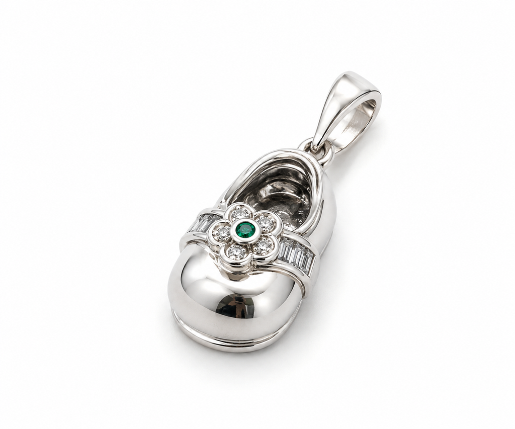 Elegant baby shoe charm pendant with green flower detail displayed beside a teddy bear and soft baby accessories.