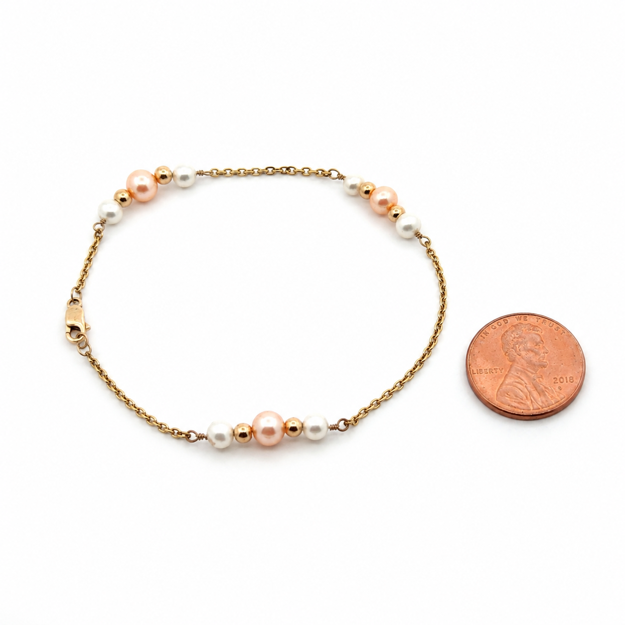 14K gold pearl bracelet with white and pink freshwater pearls shown next to a U.S. penny for accurate size reference