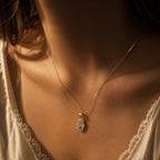 Model wearing a 14K gold Hamsa hand evil eye necklace with blue enamel accents and symbolic protection charm