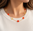 Delicate gold disc station necklace featuring alternating red and textured gold circular charms, elegantly displayed with flowers.