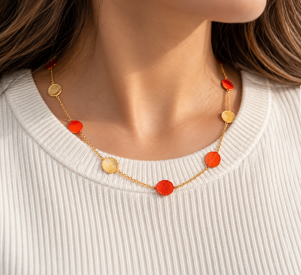 Delicate gold disc station necklace featuring alternating red and textured gold circular charms, elegantly displayed with flowers.