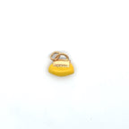 Yellow handbag-shaped jewelry charm with gold-tone details, displayed on natural beige stone beside delicate white flowers.