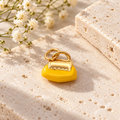 Yellow handbag-shaped jewelry charm with gold-tone details, displayed on natural beige stone beside delicate white flowers.