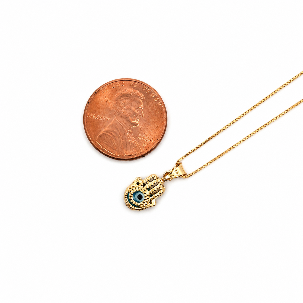 14K gold Hamsa hand evil eye pendant necklace with blue enamel accents displayed next to a U.S. penny for size comparison