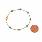 14K gold blue evil eye bracelet with blue enamel charms shown beside a U.S. penny for size comparison