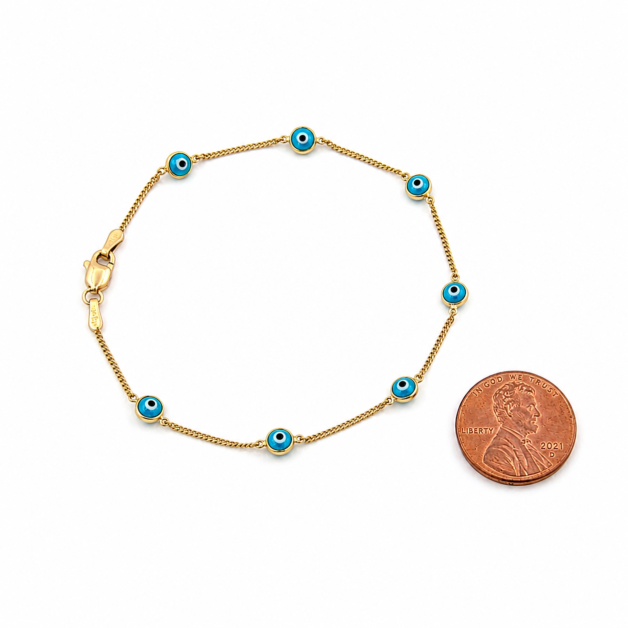 14K gold blue evil eye bracelet with blue enamel charms shown beside a U.S. penny for size comparison