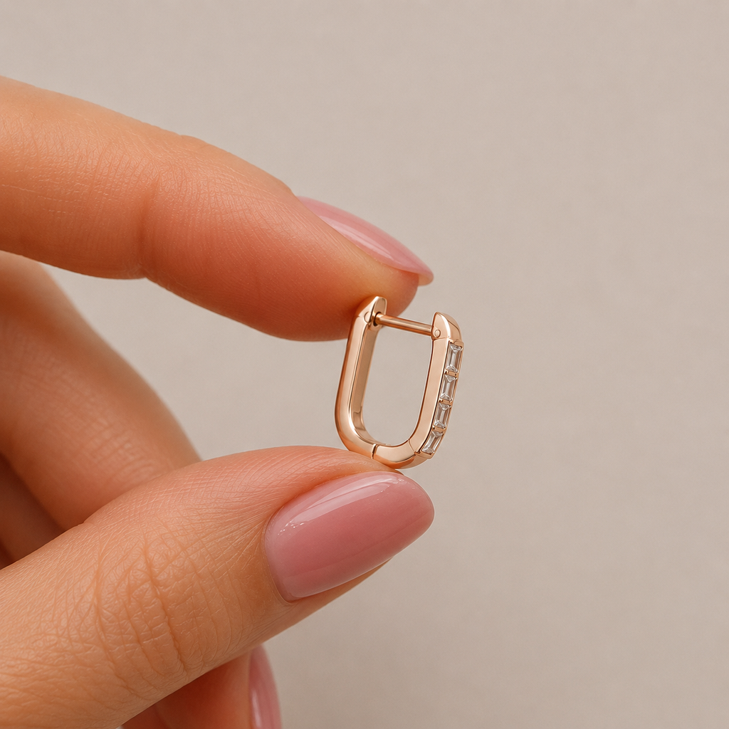 Close-up of 18K yellow gold baguette diamond huggie earring held by hand for size reference, featuring natural baguette-cut diamonds