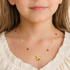 Child wearing a gold bee necklace with red and yellow teardrop charms