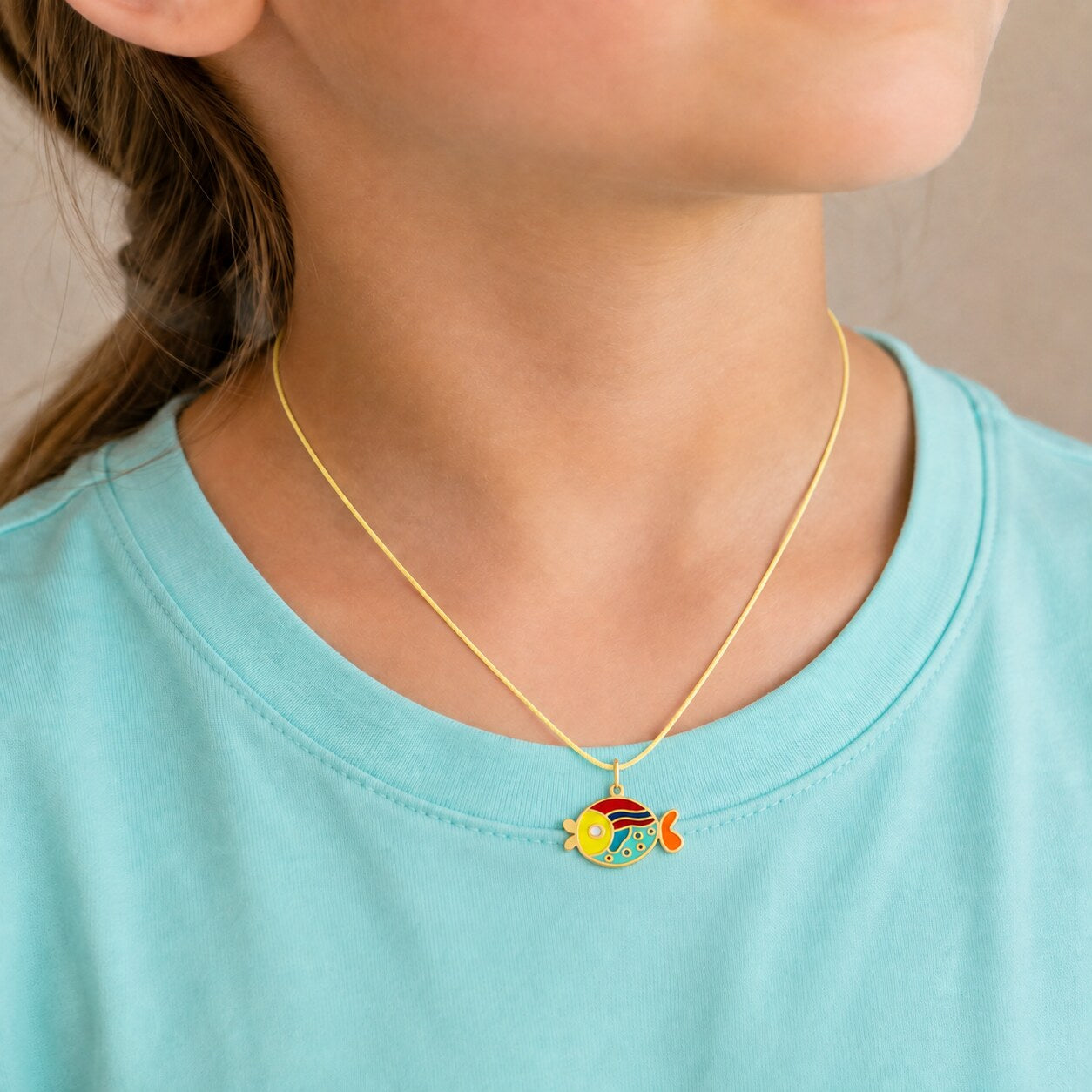 Child wearing a small colorful gold fish pendant on a yellow cord