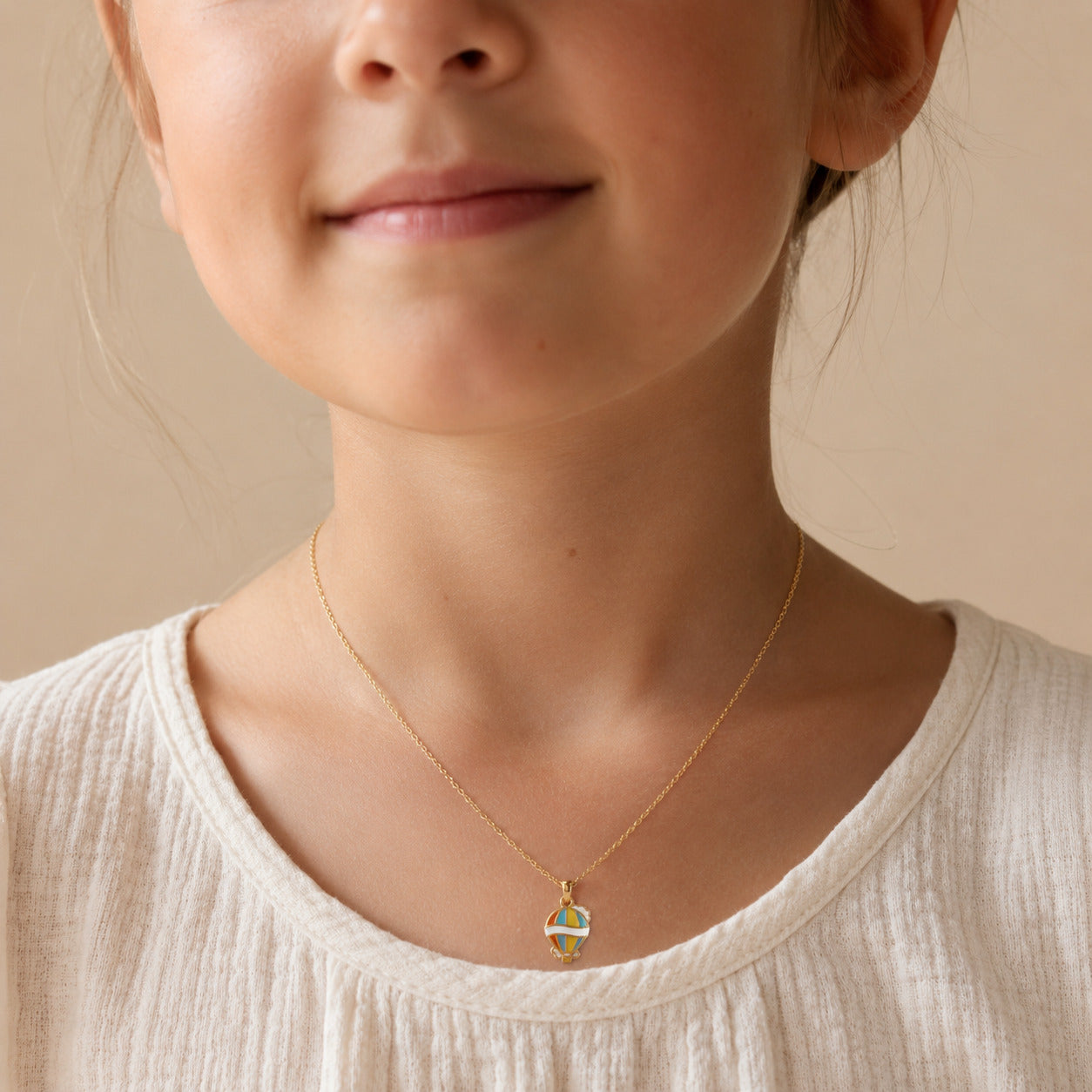 Child wearing a gold necklace with a colorful hot air balloon pendant