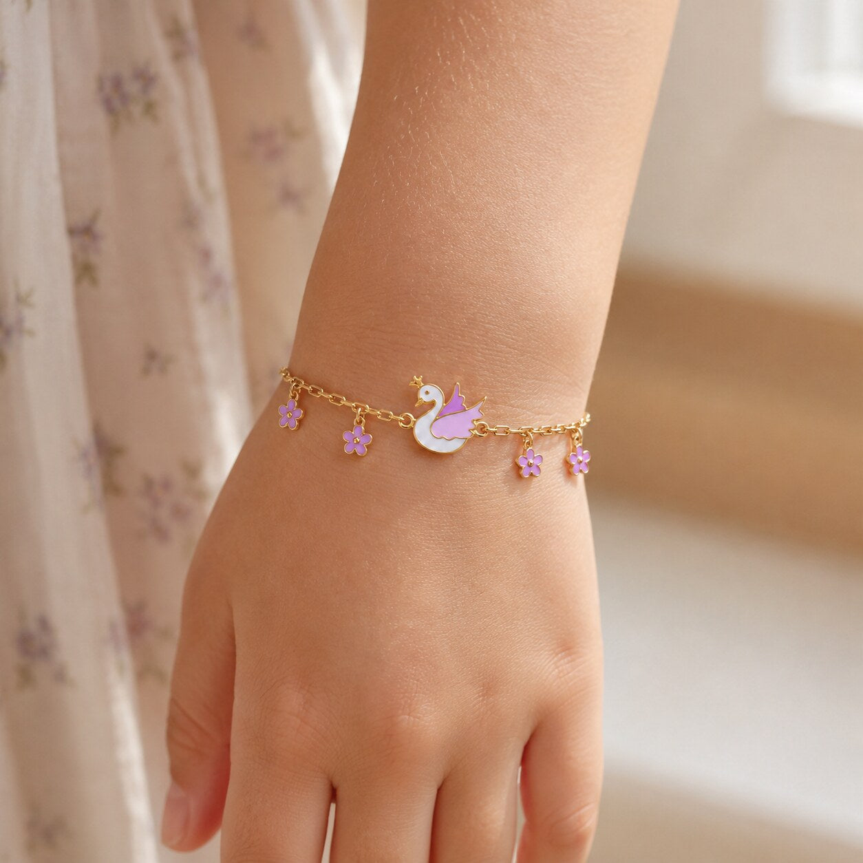 Child wearing a delicate gold crowned swan and purple flower bracelet