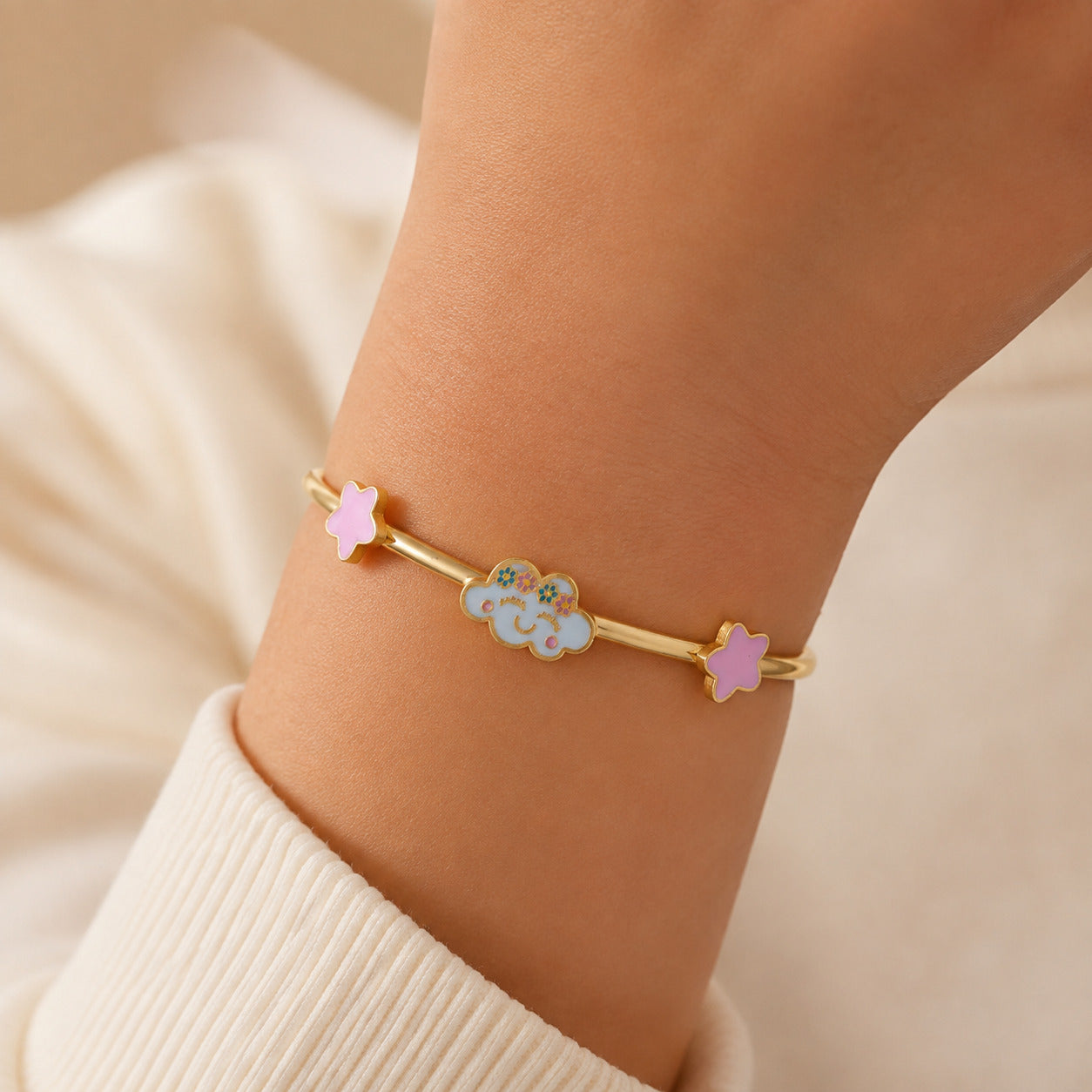 Child wearing a gold bangle with a smiling cloud and pink star accents
