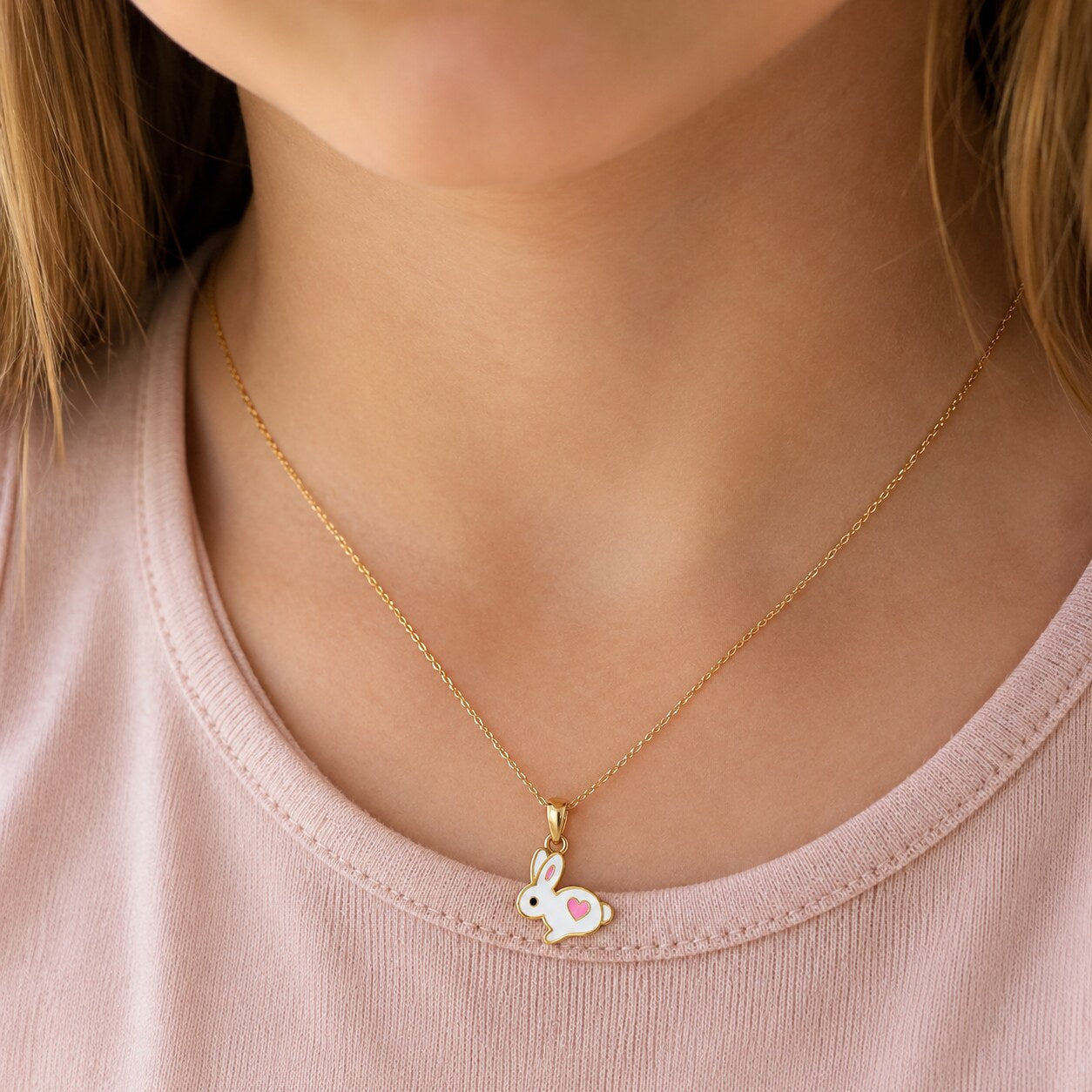 Child wearing a small gold white bunny and pink heart necklace