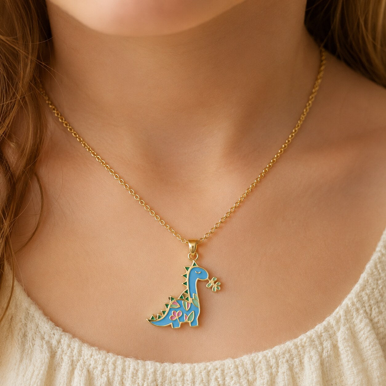 Child wearing a yellow gold necklace with a small colorful dinosaur pendant