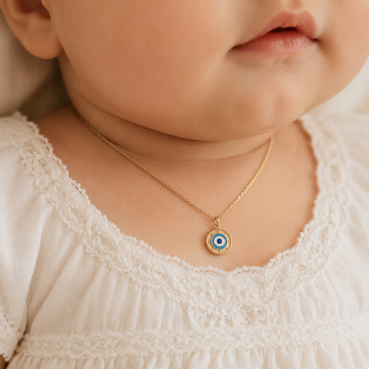 Petite yellow gold blue evil eye pendant styled on an infant model