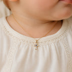 Petite yellow gold and white cross pendant styled on an infant model