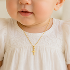 Small 14K yellow gold cross pendant worn by a baby in baptism attire